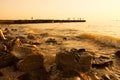 Summer, beach sunset by the sea. In the background, a breakwater from which people jump into the ram. On front huge stones, surf. Royalty Free Stock Photo