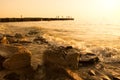 Summer, beach sunset by the sea. In the background, a breakwater from which people jump into the ram. On front huge stones, surf. Royalty Free Stock Photo