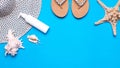 Summer beach vacation flatlay. Sunhat, seashells, female sandals, lotion and starfish on blue background, copy space. Royalty Free Stock Photo