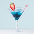 Summer blue alcohol cocktail with curacao  with strawberry red straw on light pastel green background and white wood table, square Royalty Free Stock Photo