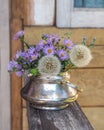 Summer bouquet of blue New Belgian asters and fluffy dandelions in a metal sugar bowl Royalty Free Stock Photo