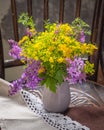 Summer bouquet of yellow and purple wild flowers in an earthenware gray vase on an old chair in a rustic interior Royalty Free Stock Photo