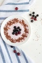 Summer breakfast with berries. A plate with yogurt, chocolate, blackcurrants and gooseberry on a light background. Vertical photo