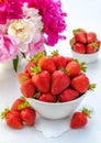 Summer breakfast concept. Fresh strawberries in a bowl on the table and a bouquet of peonies in a vase