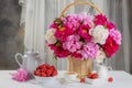 Summer breakfast concept. Fresh strawberries in a bowl on the table and a bouquet of peonies in a vase