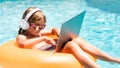 Summer business. Kid remote working on laptop in pool. Little business man working online on laptop in summer swimming