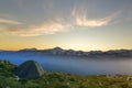 Summer camping in mountains at dawn. Tourist tent on round grassy hill on distant misty blue mountains range under pink sky before Royalty Free Stock Photo