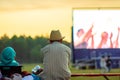 Summer cinema. A man in a straw hat is watching a movie in the open air