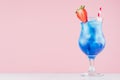 Summer cold blue lagoon alcohol cocktail with curacao liquor, strawberry slice, ice cubes, straw in misted glass on pink. Royalty Free Stock Photo