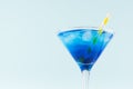 Summer cold blue lagoon drink with ice cube, yellow striped straw in elegant martini glass on pastel mint background, closeup.