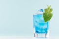 Summer cold blue lagoon drink with ice cubes, green mint in elegant shot glass on pastel mint background. Royalty Free Stock Photo