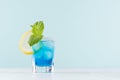 Summer cold blue lagoon drink with ice cubes, salt rim, green mint, lemon slice in elegant shot glass on pastel mint background. Royalty Free Stock Photo