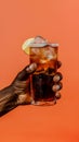 Summer concept - hand holding rum and coke cocktail, solid color background Royalty Free Stock Photo