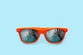 Summer concept image: orange sunglasses with palm tree reflections in pastel blue background. Royalty Free Stock Photo