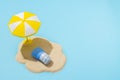 Summer concept. Sunscreen cream on sand and sun umbrella on blue background. Skin care concept in summer