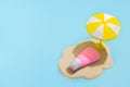 Summer concept. Sunscreen cream on sand and sun umbrella on blue background. Skin care concept in summer