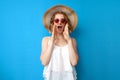 Summer concept. crazy girl in a sun hat and glasses shouts on a blue isolated background, a woman speaks loudly in summer clothes