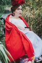 Conceptual portrait of beautiful young woman with red lips, red flowers in hair, sitting in wheel chair.