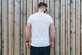 Young bearded hipster man dressed in white t-shirt and sunglasses is stands outdoor against wood wall. Mock up. Royalty Free Stock Photo