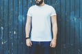 Front view. Young bearded hipster man dressed in white t-shirt and sunglasses is stands against dark wood wall. Royalty Free Stock Photo