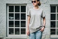 Front view. Young millennial woman dressed in gray t-shirt is stands against gray brick wall.