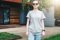 Front view. Young millennial woman dressed in gray t-shirt and sunglasses is stands on city street. Mock up. Royalty Free Stock Photo