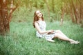 Summer day portrait of a beautiful cute young woman or girl sitting in a dress on the grass in a park with a book in her arms, sm Royalty Free Stock Photo