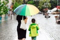 Summer day with rain. Happy family on a walk during rainy weather. Mother with big colorful rainbow umbrella Royalty Free Stock Photo