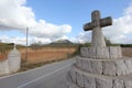 A summer day shot of an old stone cross on the side of a country road with a field with olive trees, a mountain and a blue sky Royalty Free Stock Photo
