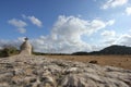 A summer day shot of an old stone cross on the side of a country road with a field with sheep, a hill, a blue sky with white