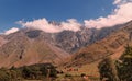 Summer day view of rocky mountains with white clouds under a blue sky hiding the mountain tops and the small houses of Royalty Free Stock Photo