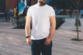 Summer day. Young bearded hipster man dressed in white t-shirt and sunglasses is stands on city street. Mock up Royalty Free Stock Photo