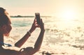 Summer days end with the best memories. a young woman using a mobile phone to take photographs at the beach. Royalty Free Stock Photo