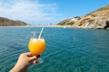 Summer drink cocktail of fresh orange juice with ice in the woman hand on the seascape background of Kolona beach