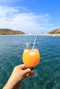 Summer drink cocktail of fresh orange juice with ice in the woman hand on the seascape background of Kolona beach