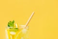 Summer drink with lemon and mint in glass with paper straw on yellow background