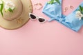 Summer essentials! Top view flat lay of blue swimsuit with sunhat, sunglasses, earrings, bracelet, and flowers on pastel pink