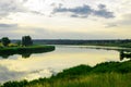 Summer evening dawn sky clouds reflected on a lake of water on the coast with green grass and forest trees Royalty Free Stock Photo