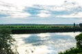 Summer evening dawn sky clouds reflected on a lake of water on the coast with green grass and forest trees Royalty Free Stock Photo