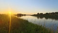 On a summer evening, the sun sets over the horizon and paints the sky in bright colors. Ripples on the water. Tall grass, bushes a Royalty Free Stock Photo