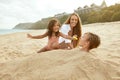 Summer. Family On Beach Having Fun. Little Girl Sharing Food With Buried In Sand Brother. Young Woman With Children. Royalty Free Stock Photo
