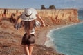 Summer fashionable girl portrait. Back view of trendy casual brunette woman in white hat resting on cliff mountains enjoying