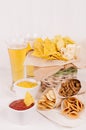 Summer fast food - different crunchy snacks and red, yellow sauce in white bowls, cold beer on soft white wood board, vertical.