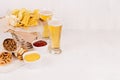 Summer fast food - different crunchy snacks and red, yellow sauce in white bowls, cold beer on soft white wood board, copy space.