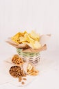 Summer fast food - different crunchy snacks in wicker rustic basket and craft paper cornet on soft white wood board, closeup.