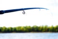 Summer fishing. A fragment of a fishing rod on the background of the shore with green trees. Selective focus