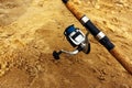 Summer fishing. A fragment of a spinning rod with a spinning reel on the background of a sandy shore. Copy space