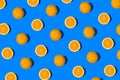 Summer flat lay pattern made with fresh whole orange fruit and slices on vibrant blue background. Minimal sunlight concept with
