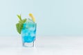 Summer fresh blue curacao cocktail with lemon slice, ice cubes, mint in wet shot glass on white wood table, pastel green. Royalty Free Stock Photo