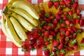 Summer fresh fruits, a lot of ripe strawberries and big bunch of yellow bananas, on yellow kitchen towel